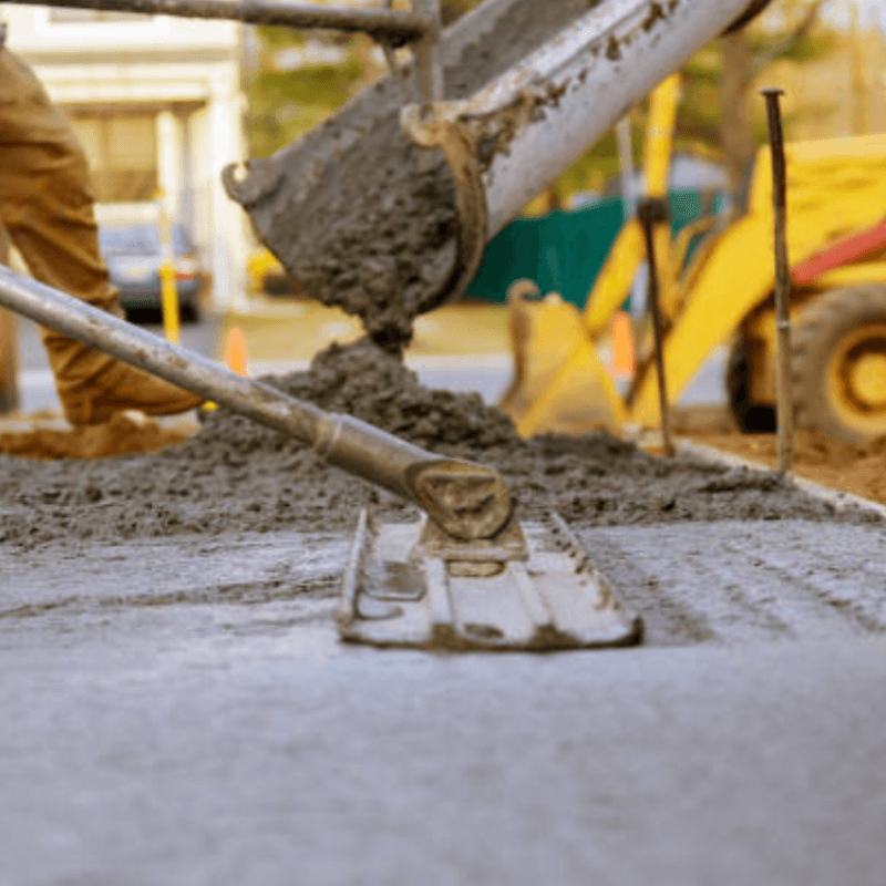 Wet concrete being poured and smoothed with a float tool at a construction site.